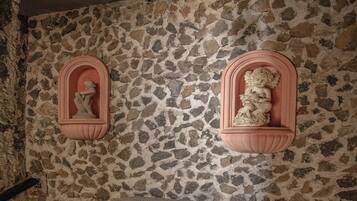 A stone wall with two pink-framed niches containing statues, a fireplace with a stone mantle, and potted plants.