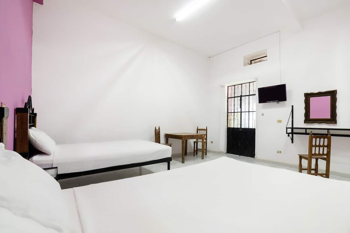 A room with two beds, a table, chairs, a TV, and a door with a window.