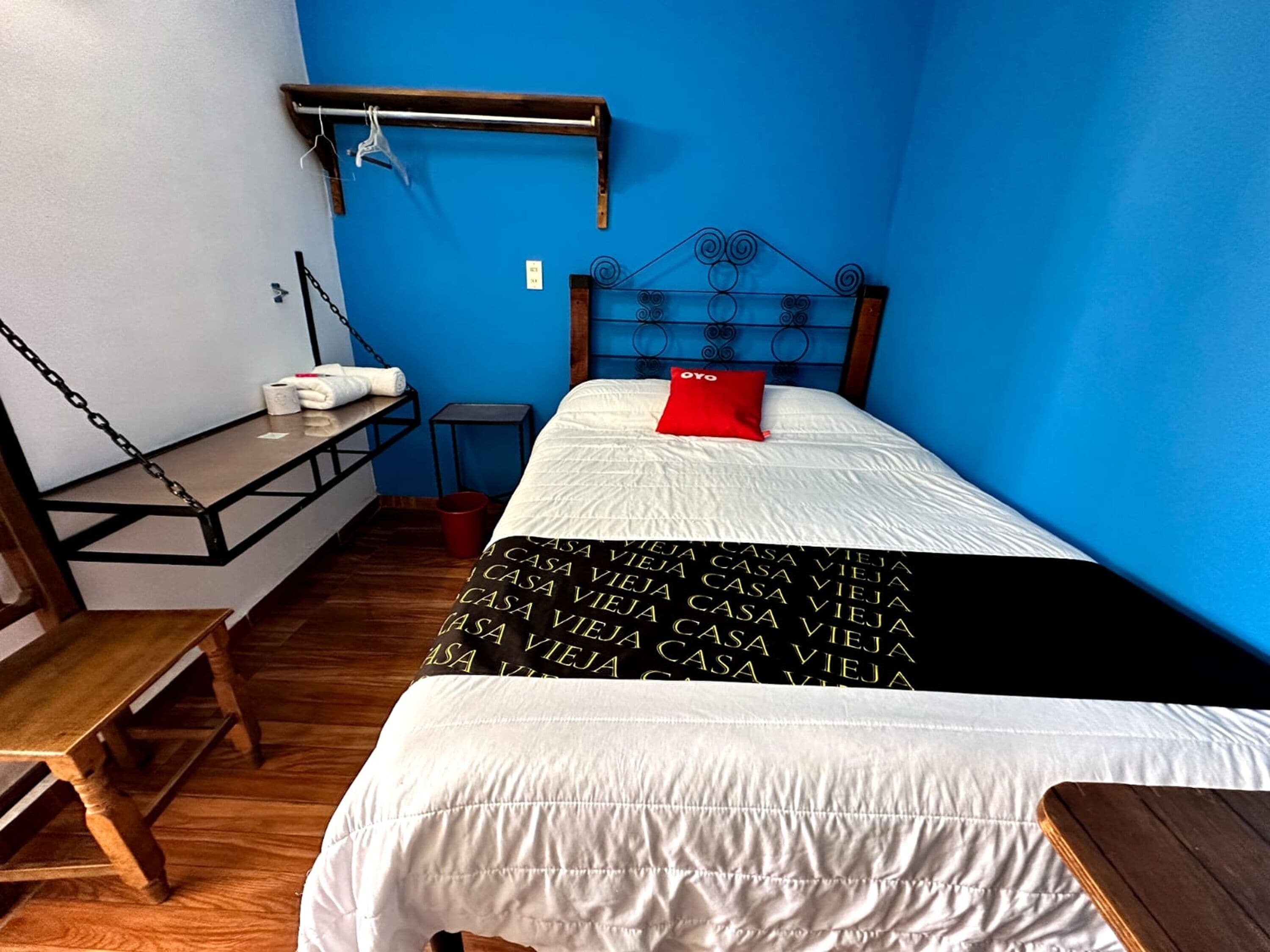 A bedroom with a bed, a wooden bench, a small table, and a red pillow.