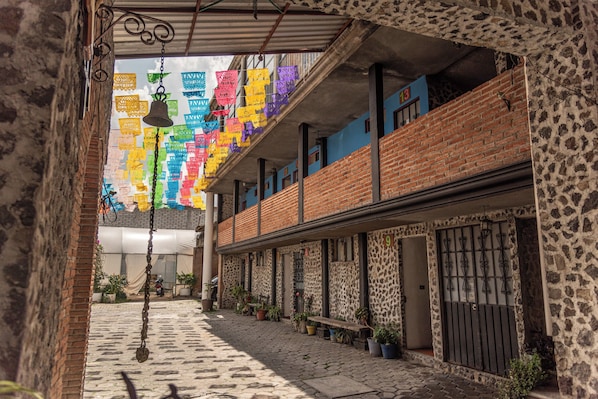 A narrow alleyway with a brick building, potted plants, and hanging decorations. - OYO Casa Vieja,Ciudad Serdán,Museo La Magnolia (Chalchicomula de Sesma)