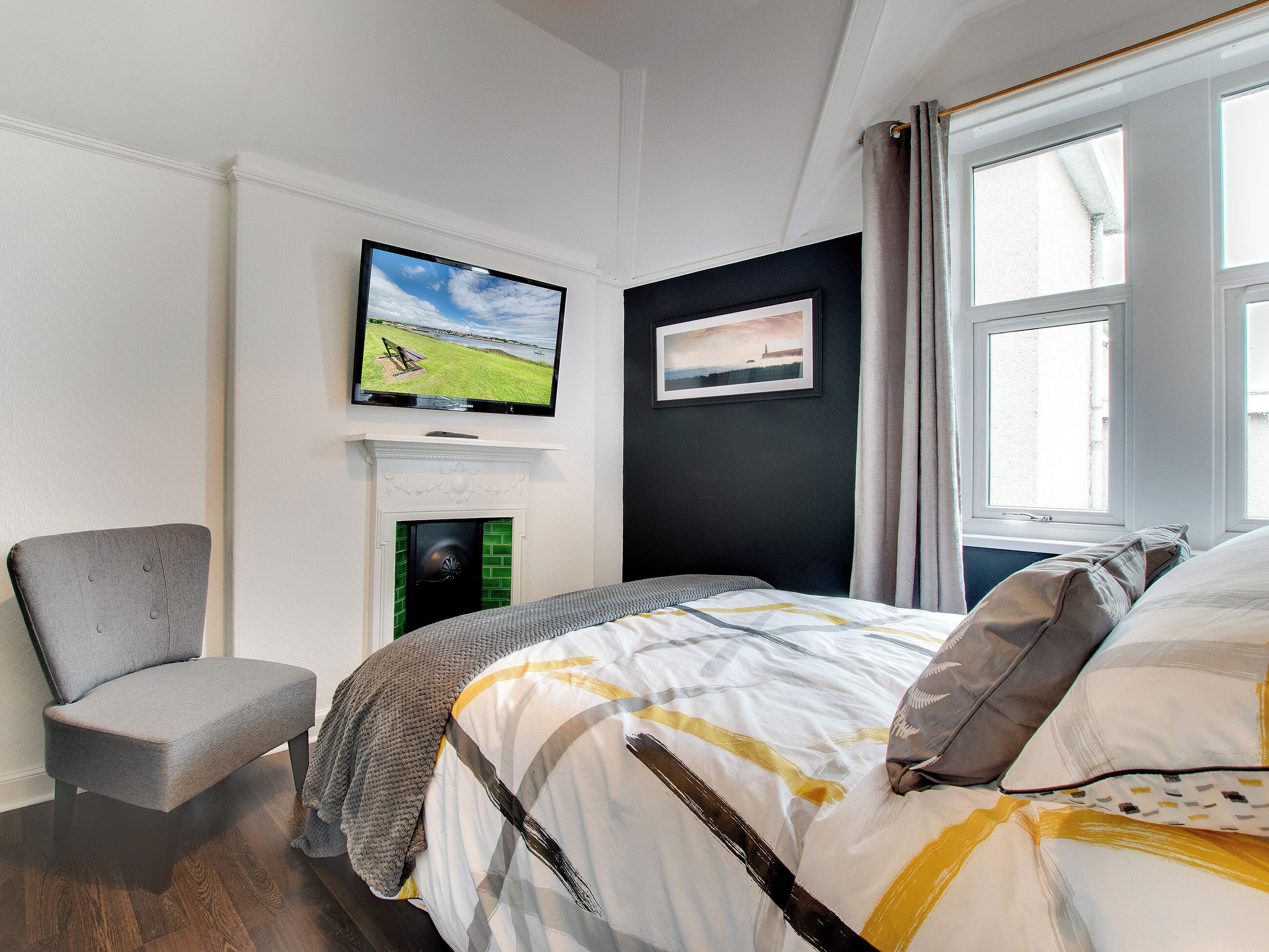 Ein Schlafzimmer mit Bett, Sessel, Fernseher an der Wand, Kamin und Fenster.