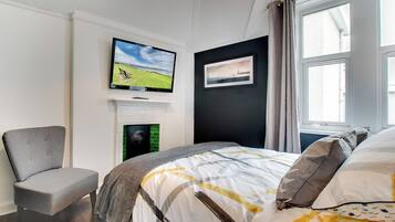 Ein Schlafzimmer mit Bett, Sessel, Fernseher an der Wand, Kamin und Fenster.