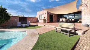 A pool area with a wooden bench and chairs, a brick building, and a large shade sail. - Luxe & Spacious Gem: Pool ~ 15min to Downtown ~ Parking! (Tucson)