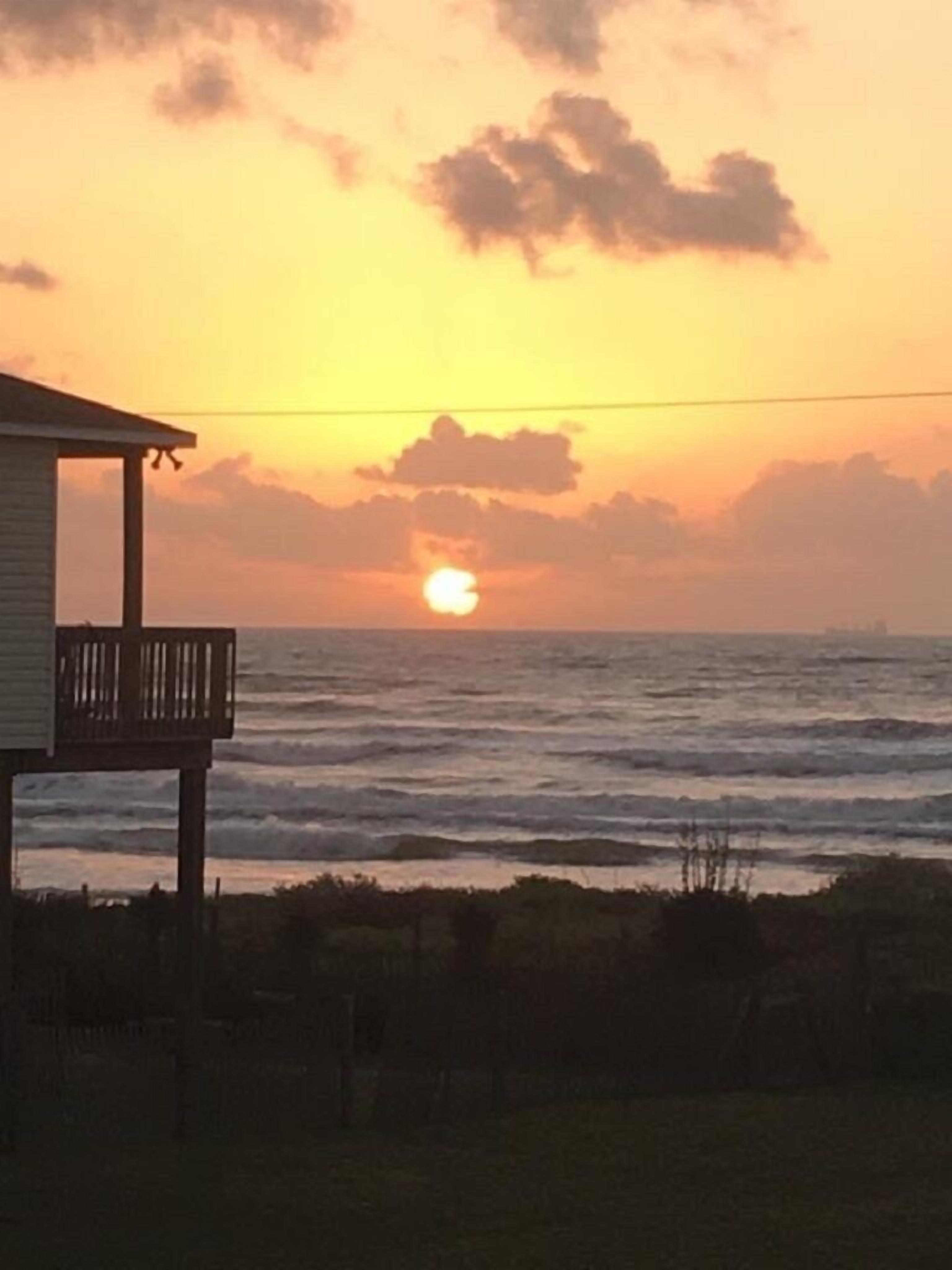A beach house with a balcony overlooking the ocean at sunset.