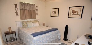 Ein Schlafzimmer mit einem Bett, einem Nachttisch, einer Lampe, einem an der Wand montierten Fernseher und gerahmten Bildern.