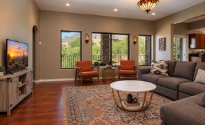 A spacious living room with a large window, a flat-screen TV, a sofa, two armchairs, and a coffee table. - Beautiful Hacienda: Pool, Spa, Firepit, Outdoor playground, BBQ & Amazing Views! (Tucson)