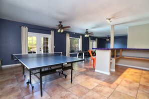 A spacious room with a ping pong table, ceiling fans, and a view through large windows. - Beautiful Hacienda: Pool, Spa, Firepit, Outdoor playground, BBQ & Amazing Views! (Tucson)