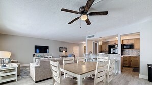 A spacious living room with a dining area, a kitchen, and a ceiling fan. - Poolside Patio | Walk to Beach (St. Pete Beach)