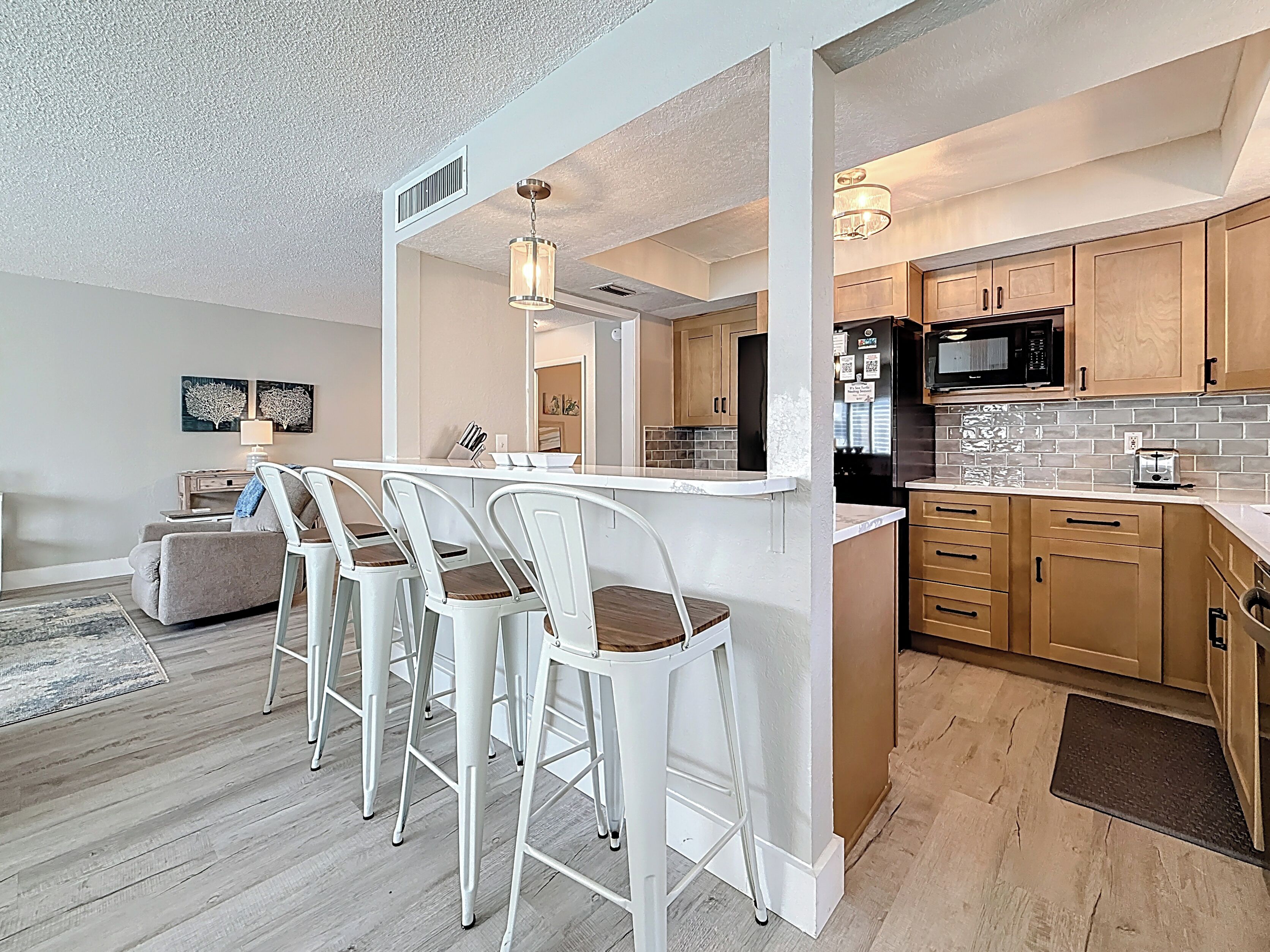 A modern kitchen with a central island, bar stools, wooden cabinets, and a microwave.