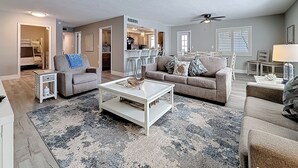A spacious living room with a large couch, a coffee table, and a dining area in the background. - Poolside Patio | Walk to Beach (St. Pete Beach)