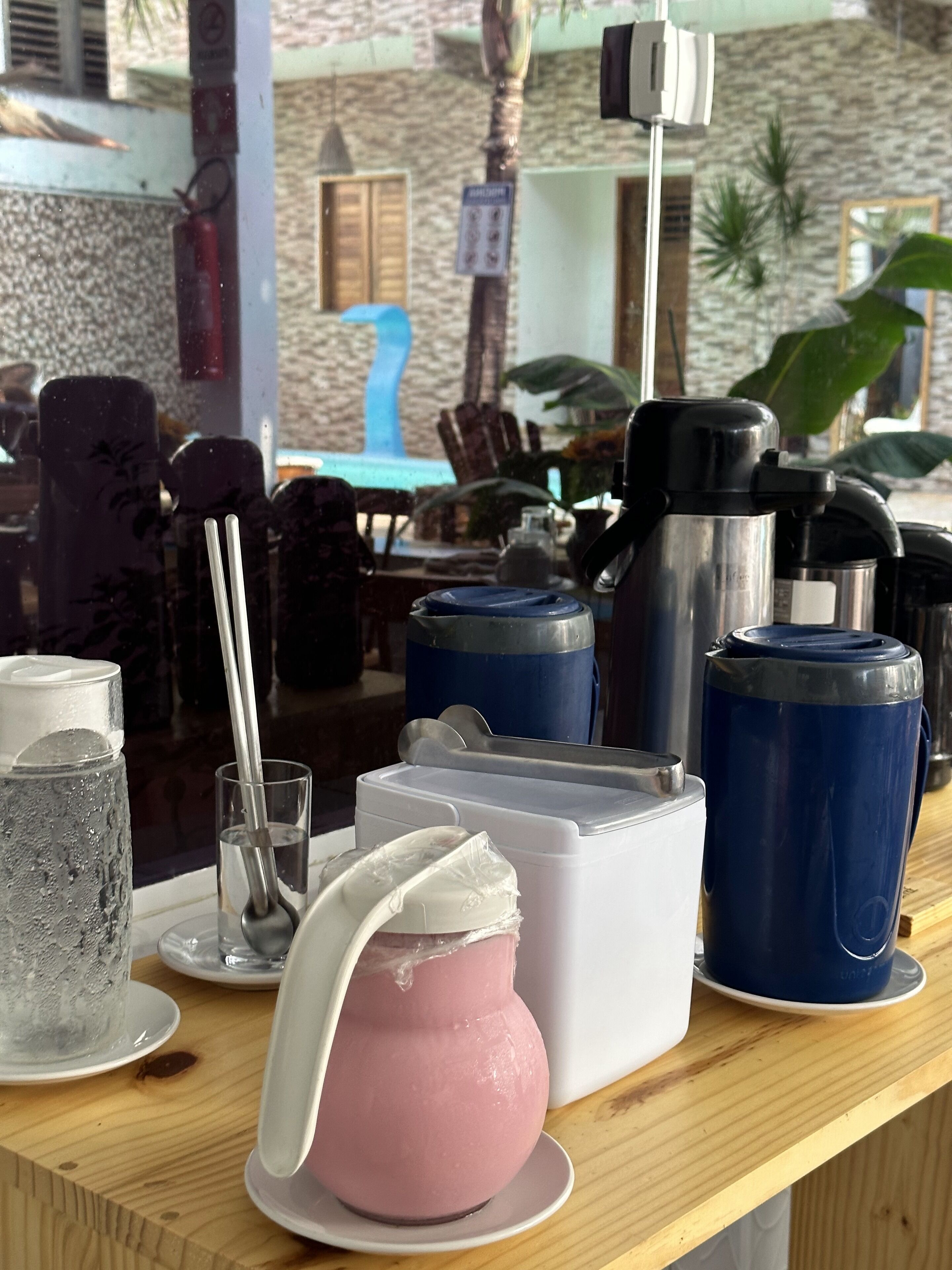 Un coin bar avec différents récipients pour les boissons, une carafe rose et un verre d’eau.