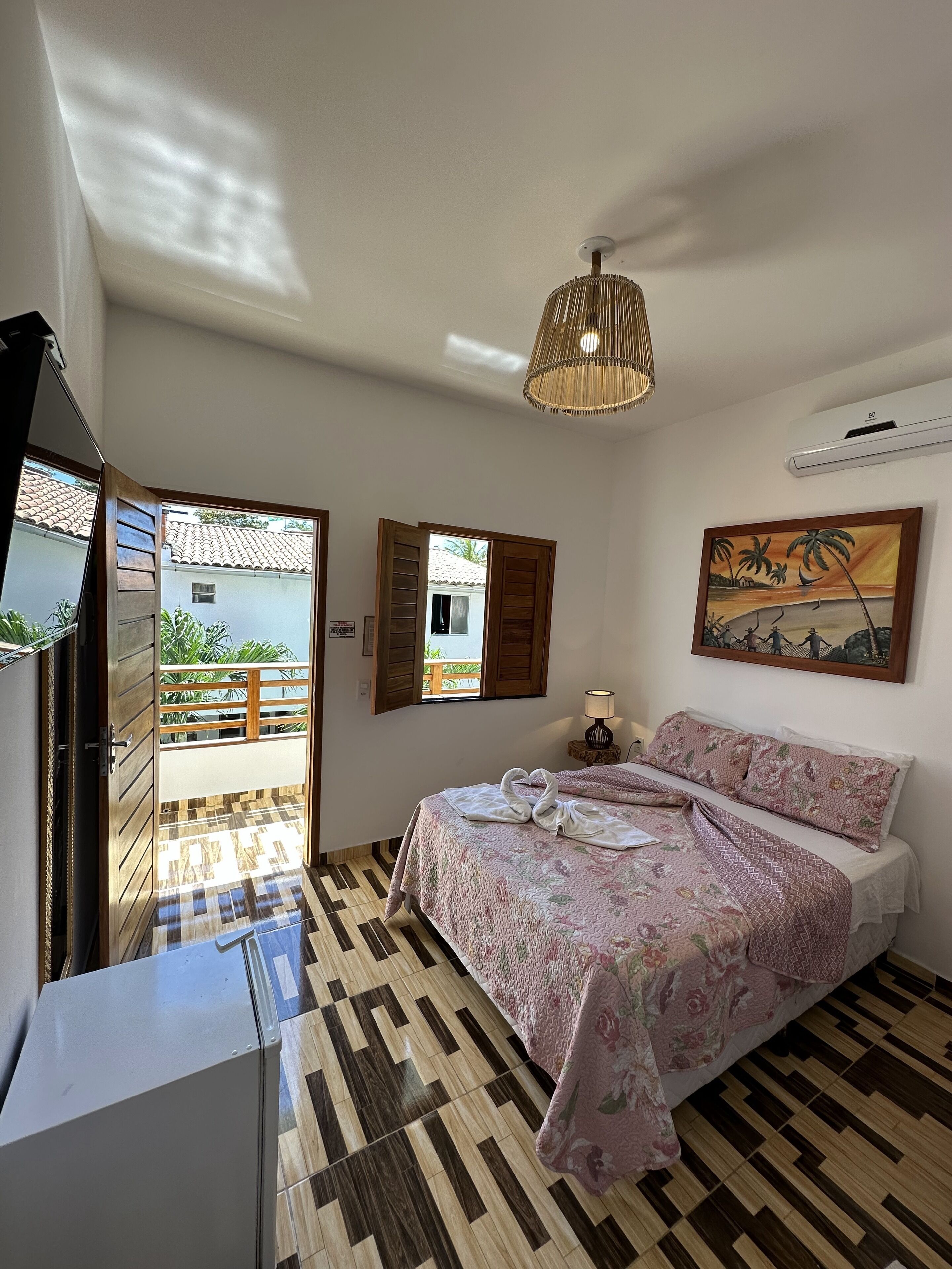 Un dormitorio con cama, un cuadro, un ventilador de techo y vistas a través de una ventana.