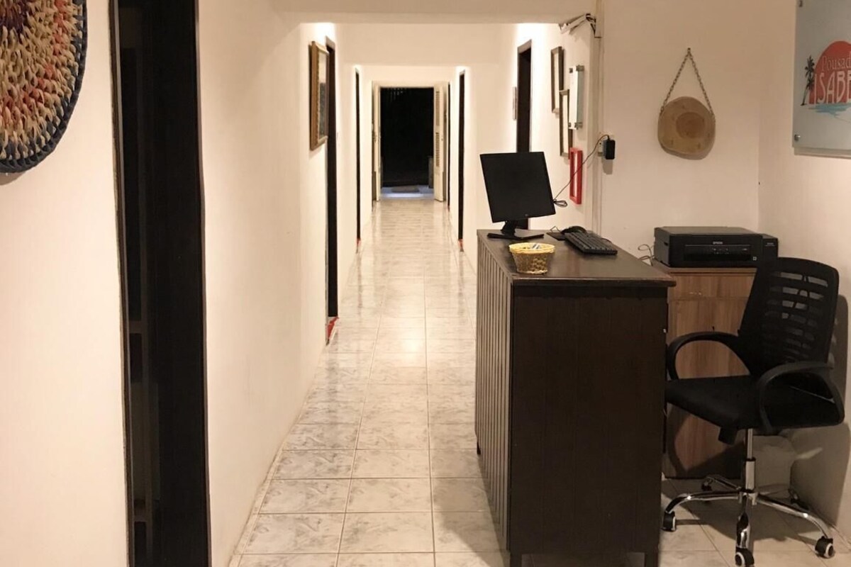Um corredor com uma mesa de recepção, um computador, uma cadeira, um relógio e uma cesta fixada na parede.