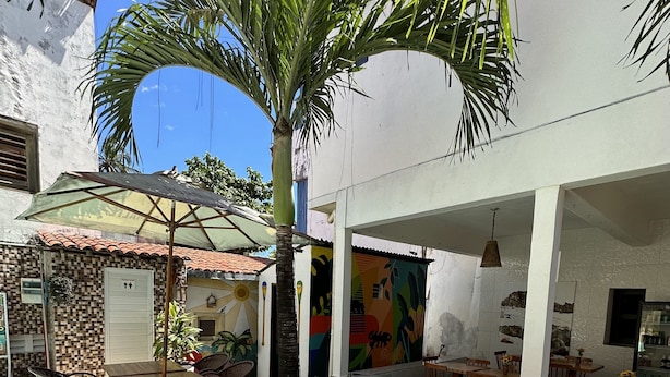 A patio area with a sun lounger, a small table with chairs, and a decorative wall with artwork. - Pousada Isabel (Jijoca de Jericoacoara)