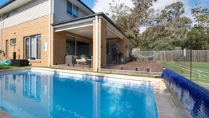 Ett modernt hus med en swimmingpool, en täckt uteplats och en inhägnad trädgård.