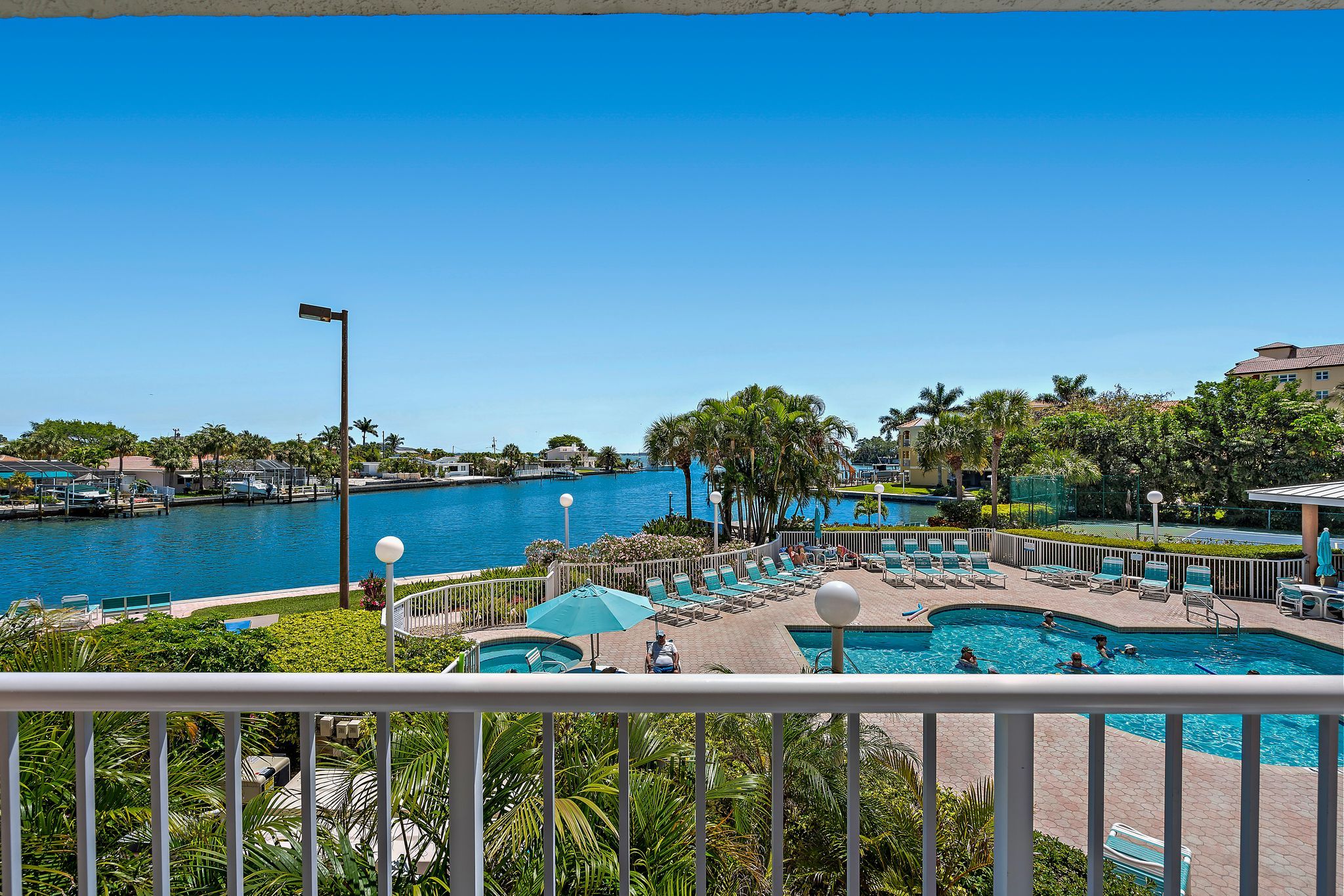 A pool area with lounge chairs and umbrellas, surrounded by palm trees and a clear blue sky.