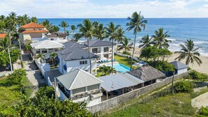A beachfront property with multiple buildings, a swimming pool, and palm trees.