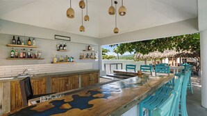 A bar area with wooden bar top, blue chairs, and shelves with bottles.