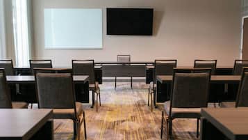 Un salón de conferencias con una gran mesa, varias sillas, una pizarra y un televisor de pantalla plana en la pared.