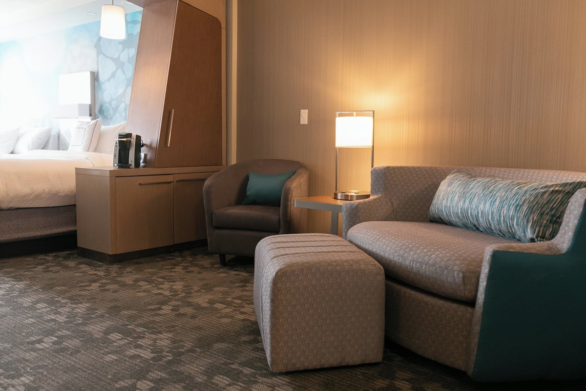 A hotel room with a bed, a desk, a chair, a sofa, and a lamp.