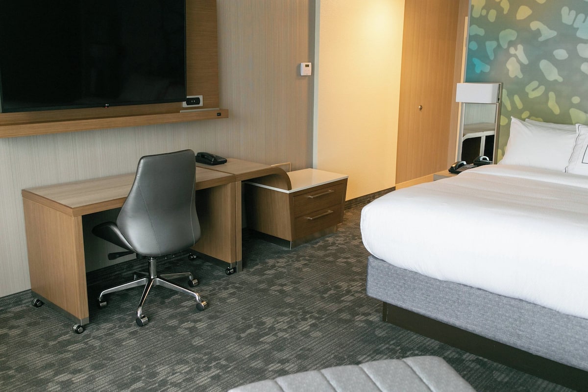 A hotel room with a bed, a desk with a chair, a television, and a bedside table.