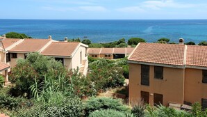 A coastal residential area with terracotta-roofed houses, lush greenery, and a view of the sea.