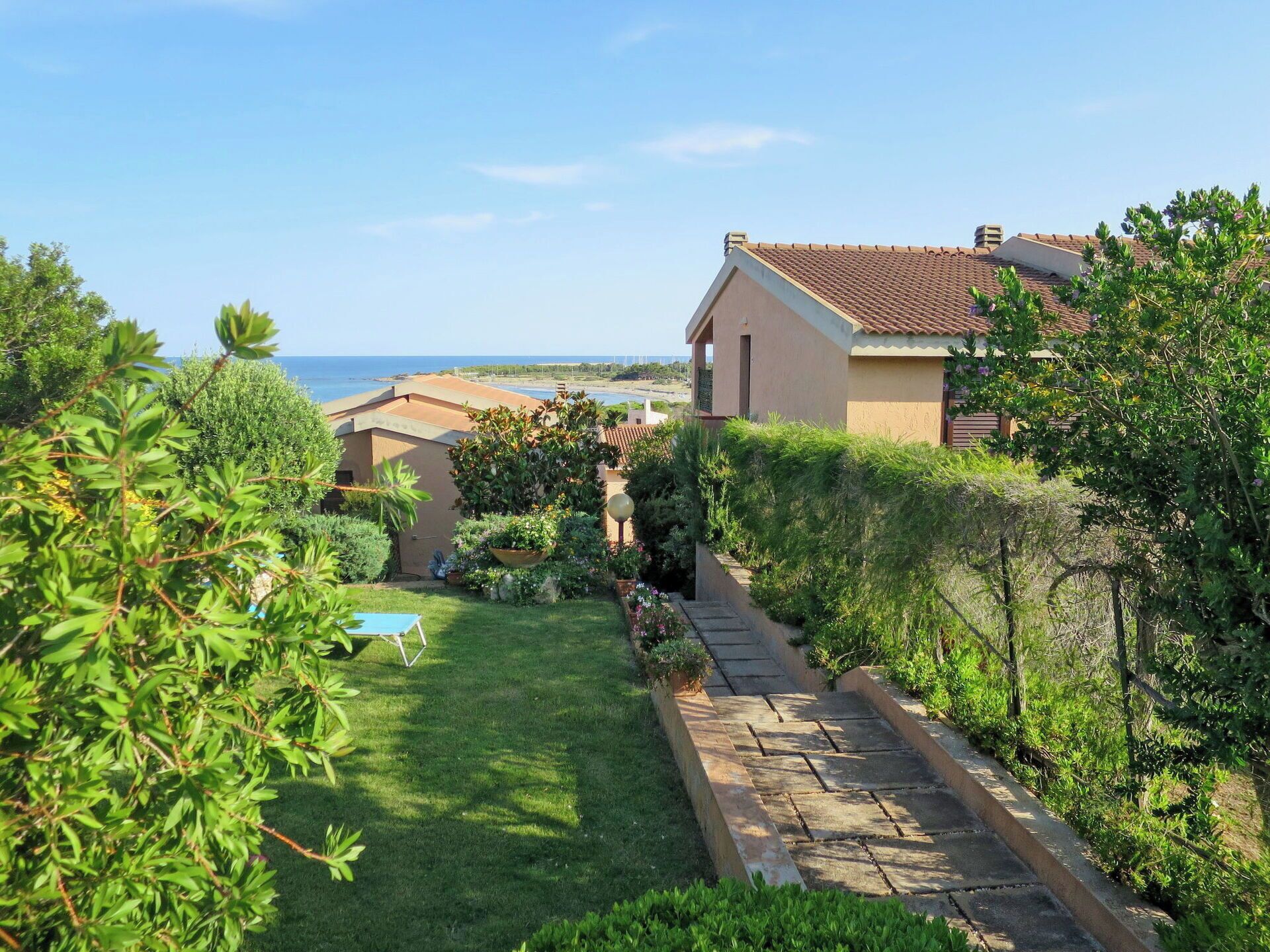 Una proprietà costiera con un giardino curato, un vialetto in pietra e vista sul mare.