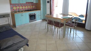 Una cucina compatta con mobili color petrolio, un fornello a gas e un'area pranzo con tavolo e sedie.