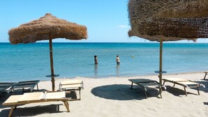 Una spiaggia con ombrelloni di paglia e lettini vista mare.