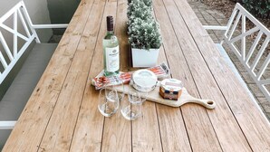 Een houten tafel met een fles, glaasjes, een kleine plant en een bakje kaasdip.