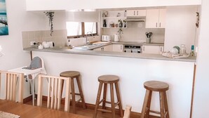 Een moderne keuken met een centraal eiland, barstoelen en een eethoek met een kinderstoel.