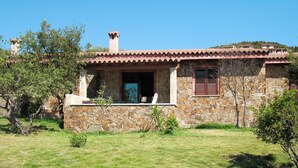 Une maison en pierre avec un toit en tuiles, une cheminée et un petit porche avec une chaise.