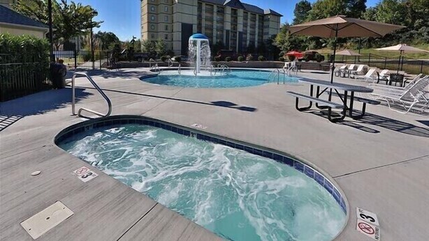 Zona de piscina con jacuzzi, sillones reclinables y sombrillas.