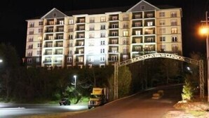 Un hotel de varios pisos con fachada simétrica, una entrada central y un área de estacionamiento con un vehículo visible.