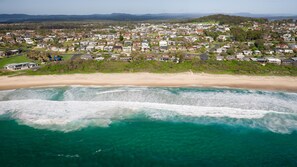 Vista aérea de una zona residencial costera con casas, una playa y olas del océano.