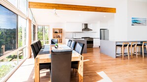 Una cucina moderna con isola centrale, zona pranzo con tavolo e sedie in legno, e ampie finestre con vista sull'esterno.