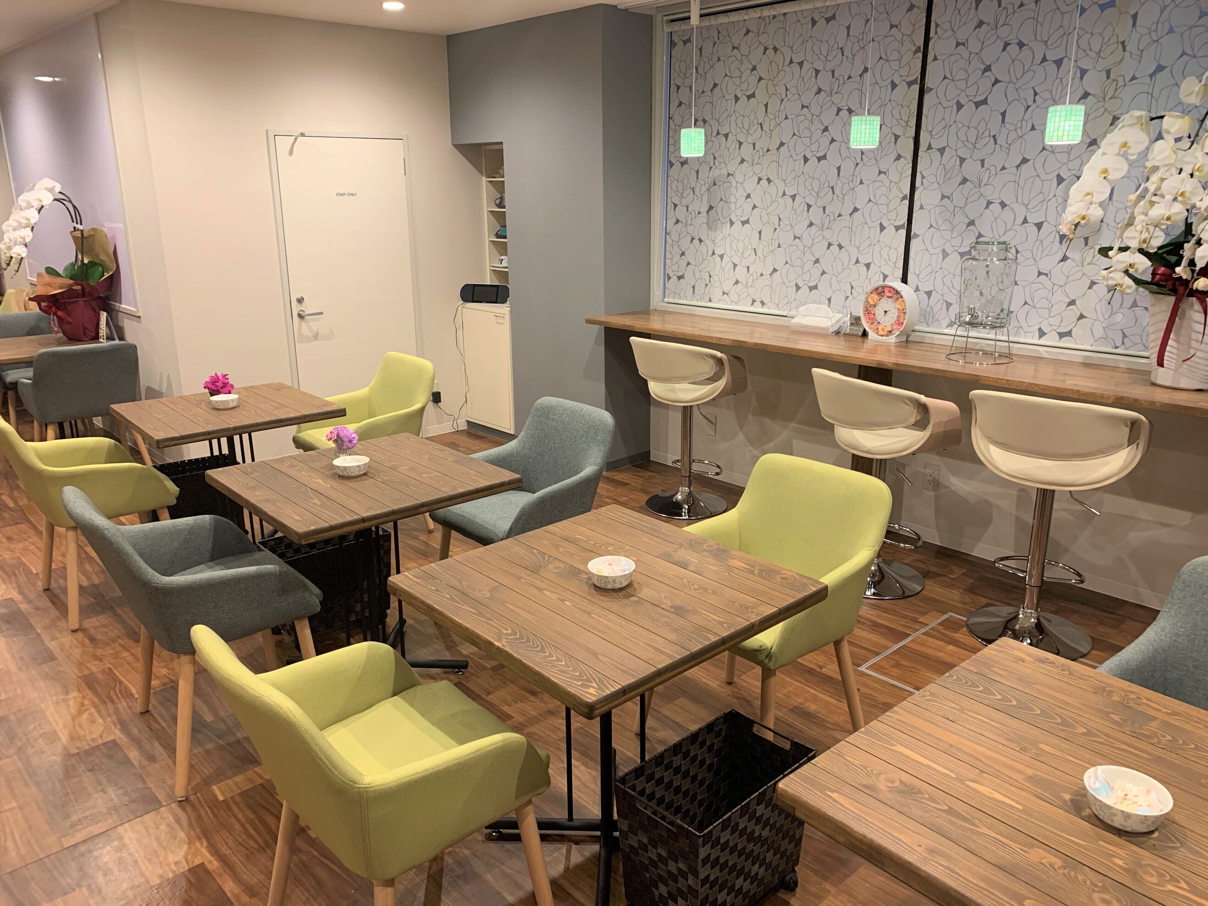 Un comedor moderno con mesas y sillas de madera, una puerta para personal exclusivo y una pared decorativa con estampado floral.