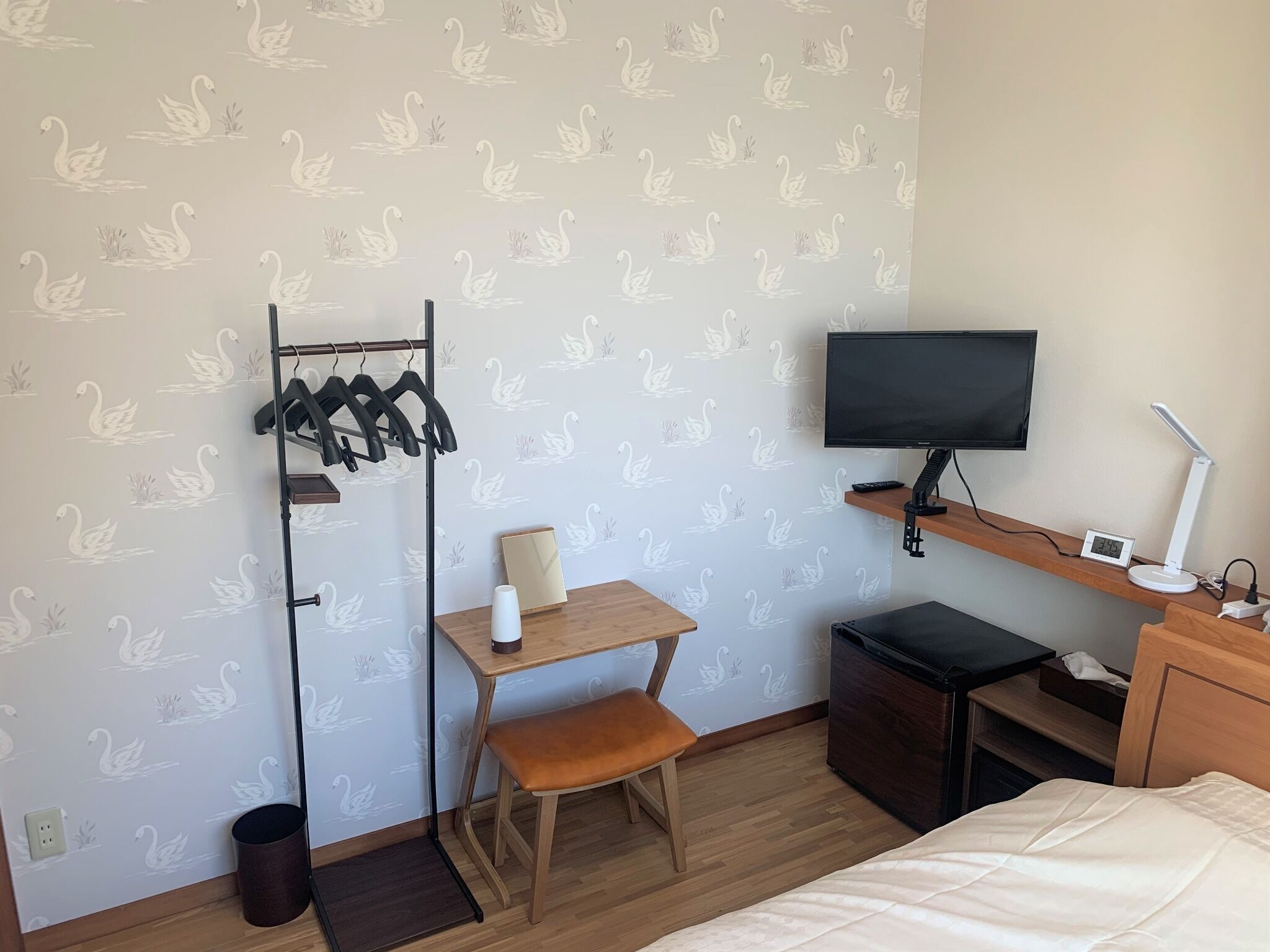 A hotel room with a desk, chair, TV, bedside table, and a bed.