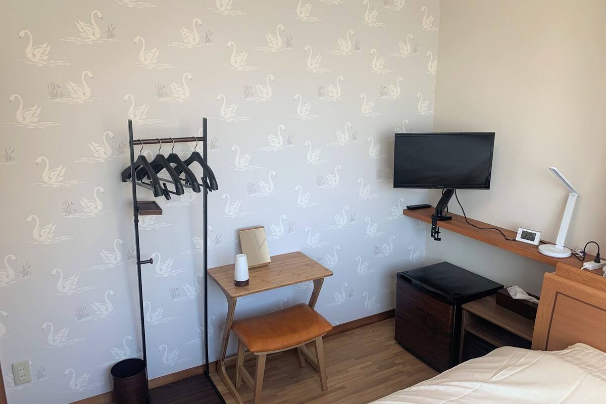 Quarto de hotel com escrivaninha, cadeira, televisão, mesa de cabeceira e uma cama.