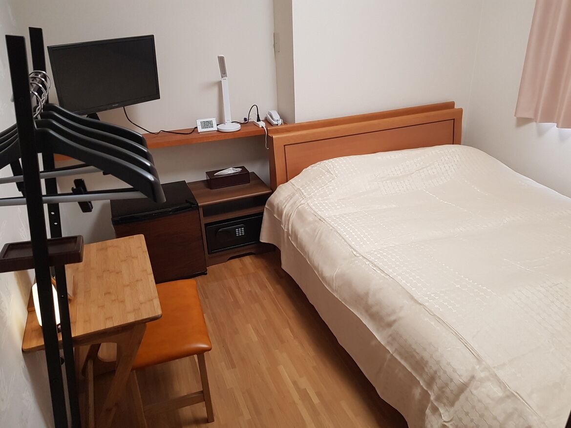 A hotel room with a bed, a desk with a chair, a TV, a lamp, and a phone on a nightstand.