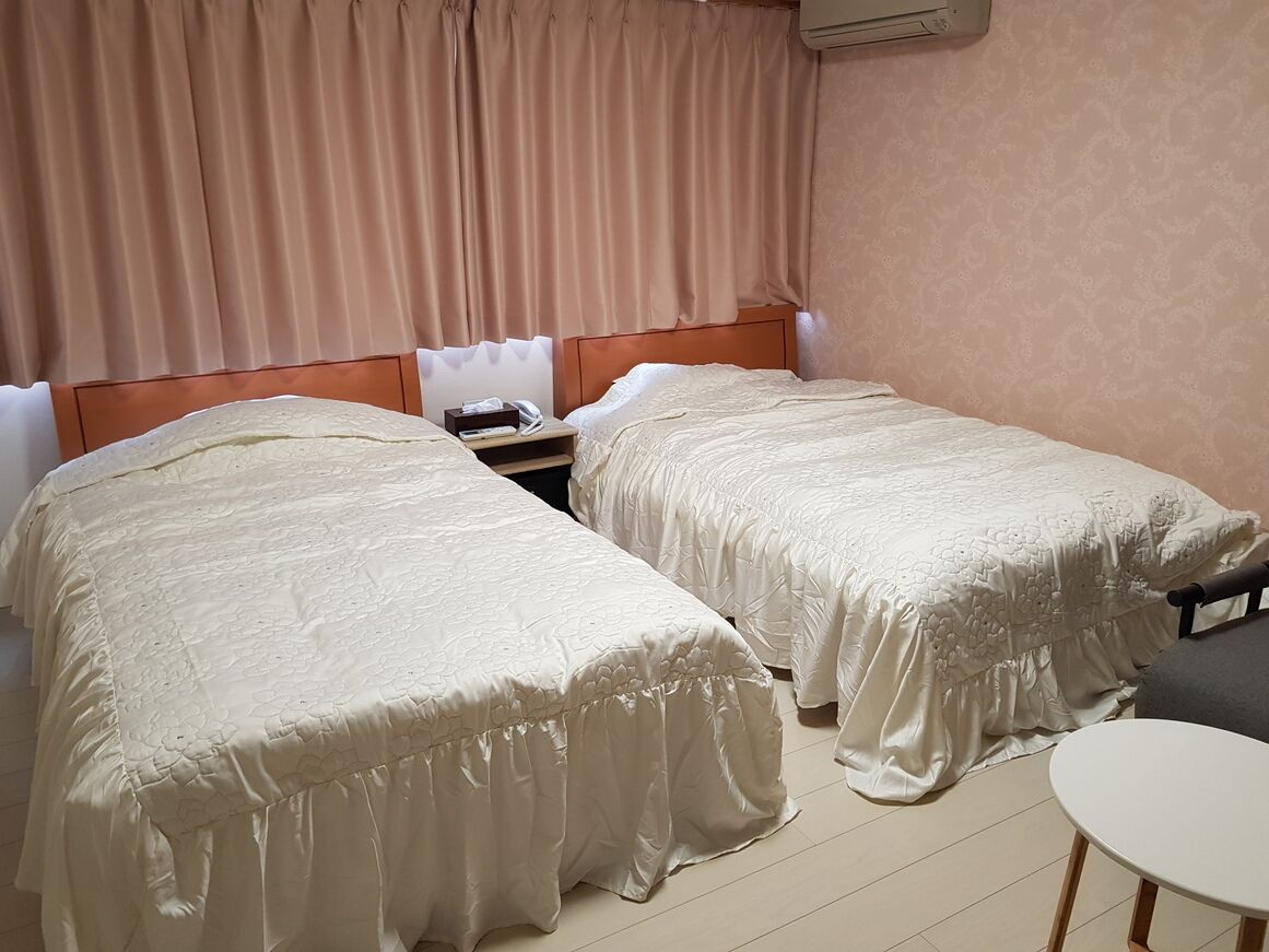 A hotel room with two beds, a bedside table, a chair, and a small table.