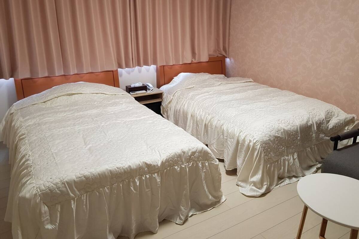 Quarto de hotel com duas camas, mesa de cabeceira, uma cadeira e uma pequena mesa.
