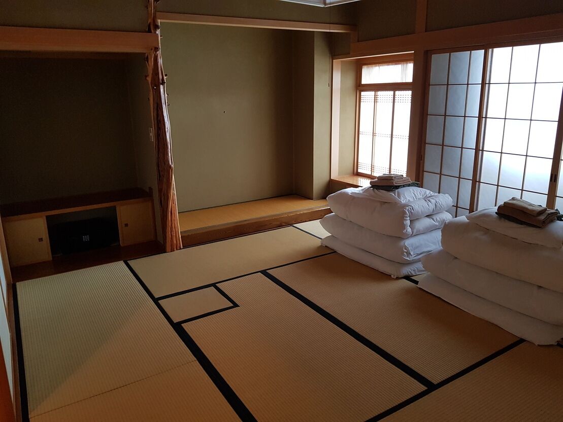 A traditional Japanese room with tatami flooring, a futon bed, a sliding door, and a window with shoji screens.