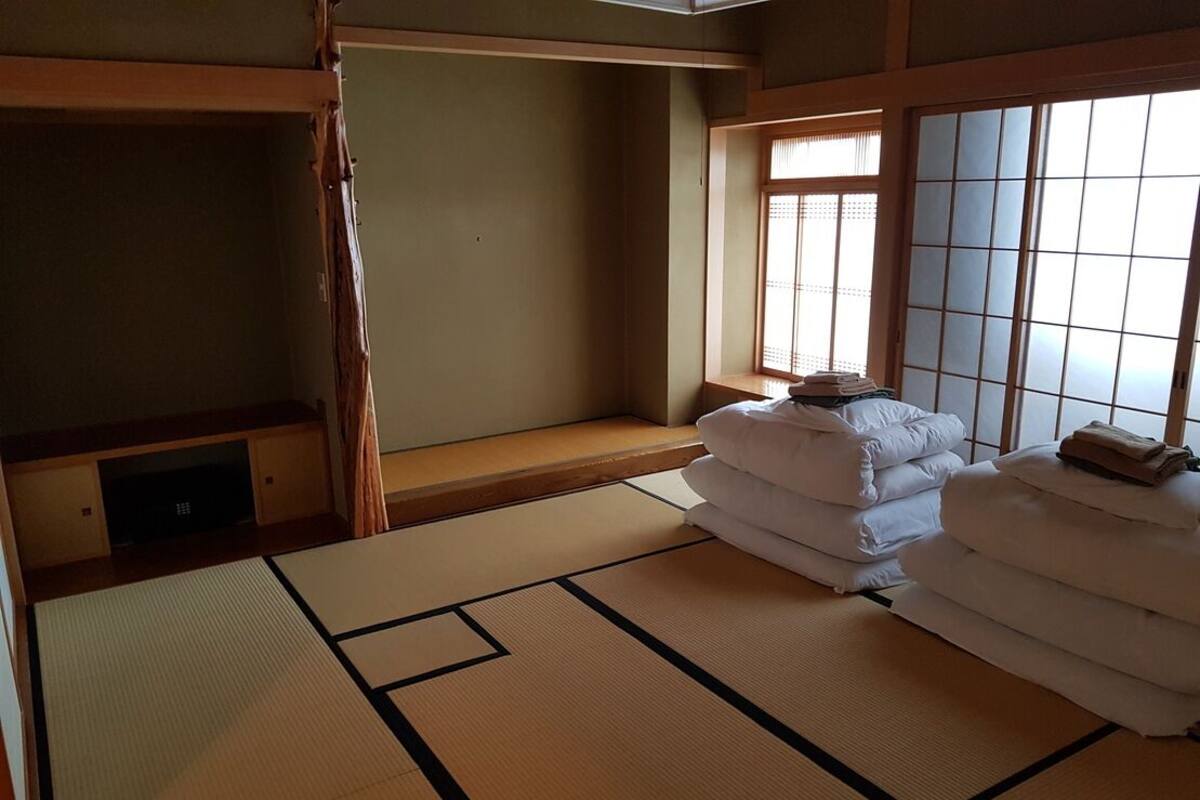 Um quarto japonês tradicional com tatames, futon, porta deslizante e janela com biombos shoji.