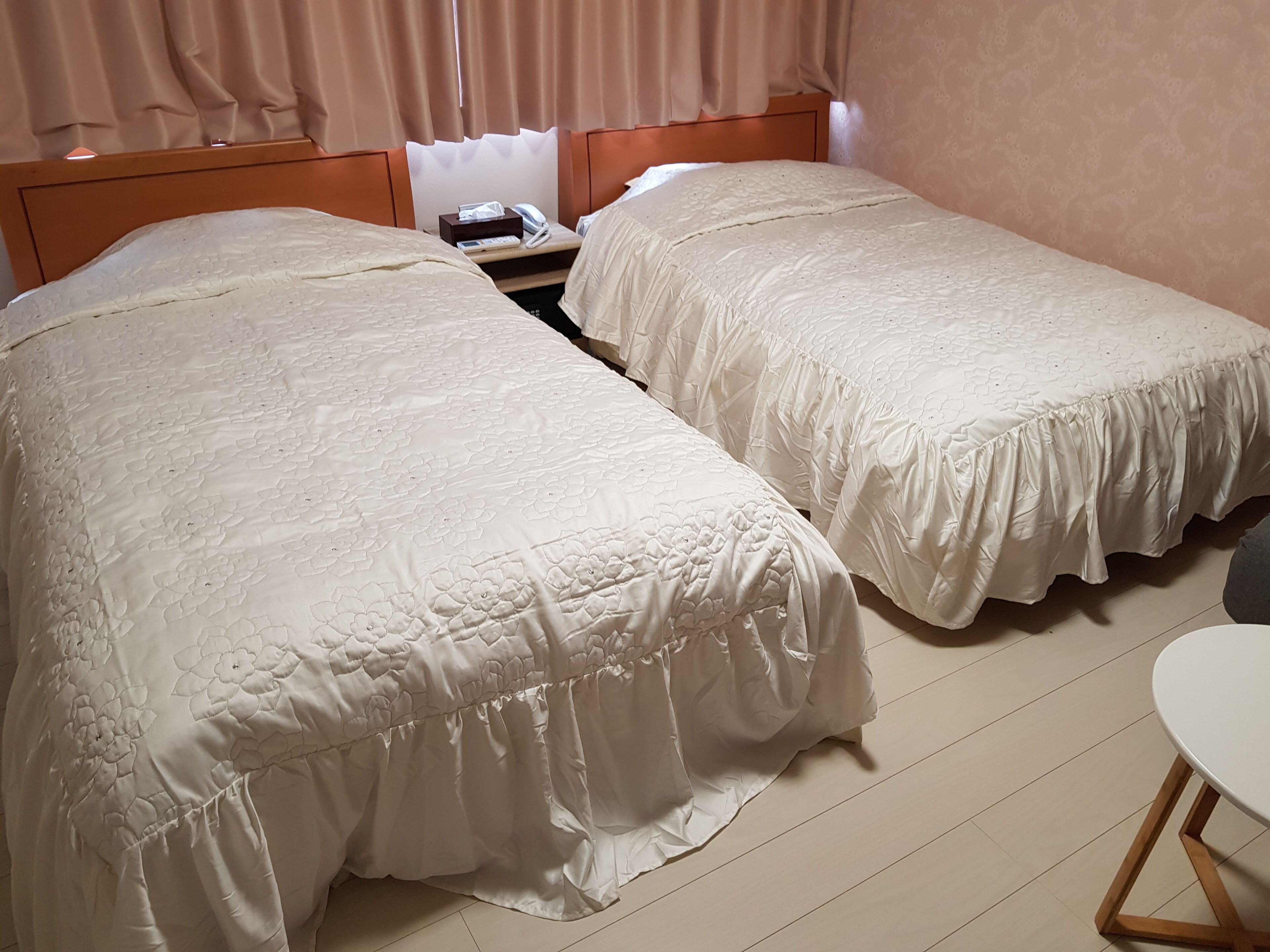 Ein Hotelzimmer mit zwei Einzelbetten, einem Nachttisch mit Telefon und Taschentüchern sowie einem kleinen Tisch mit einem Stuhl.