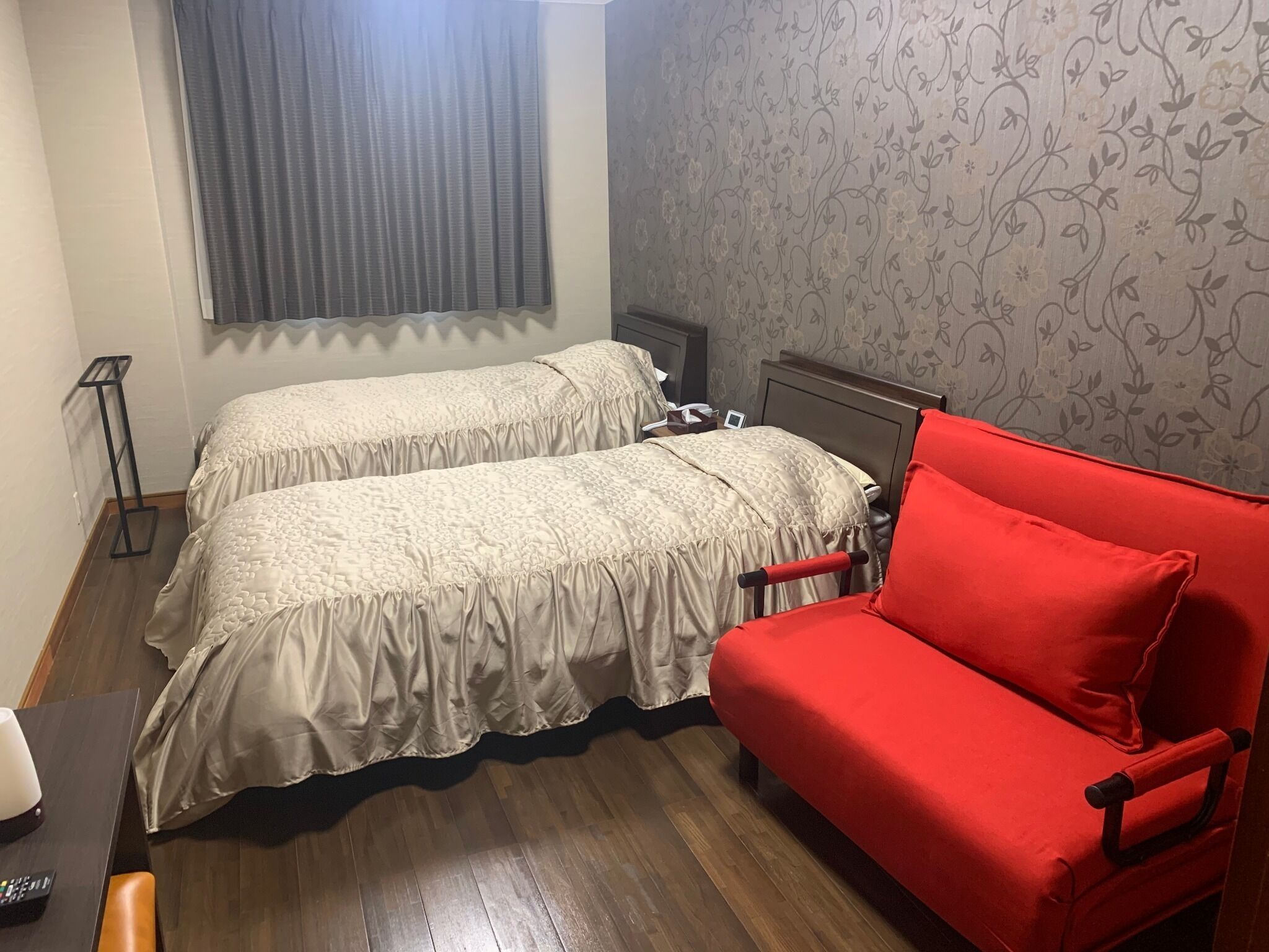 A room with two beds, a red sofa, a small table, and a window with curtains.