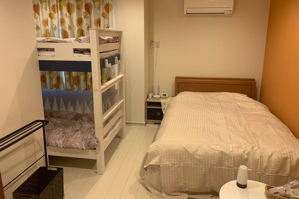 Quarto com beliches, mesa de cabeceira, luminária, ar condicionado e telefone ao lado da cama.