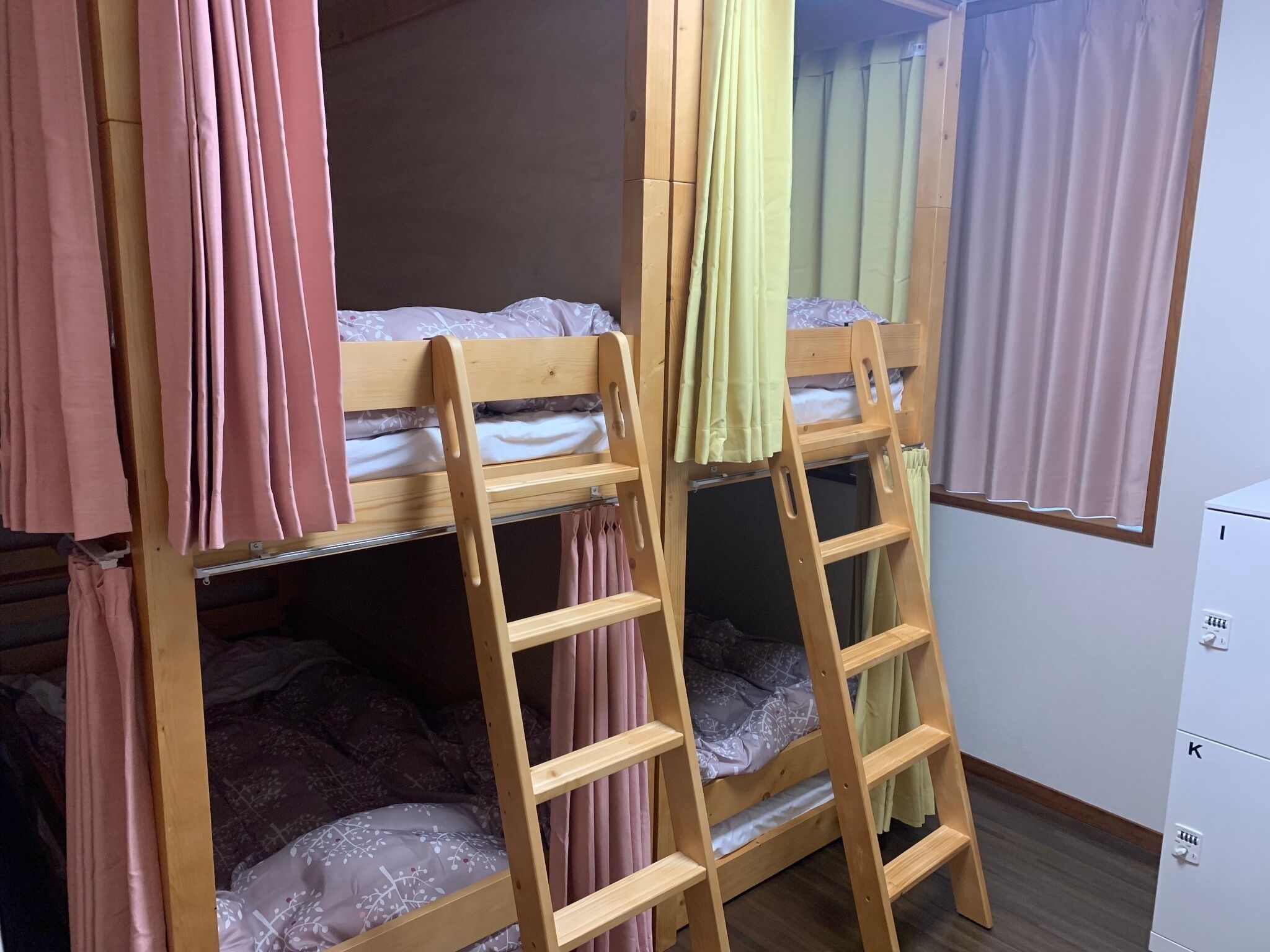A bunk bed with a ladder, pink curtains, and a white cabinet.