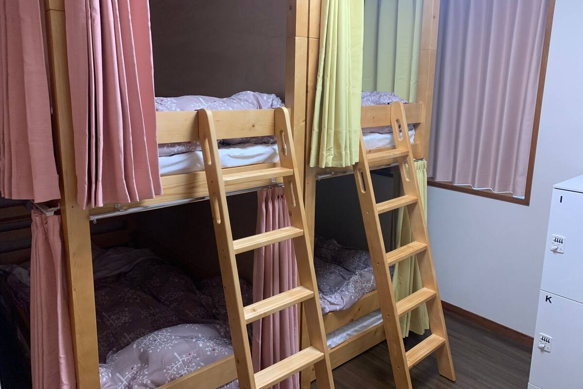 Uma cama beliche com escada, cortinas cor-de-rosa e um armário branco.