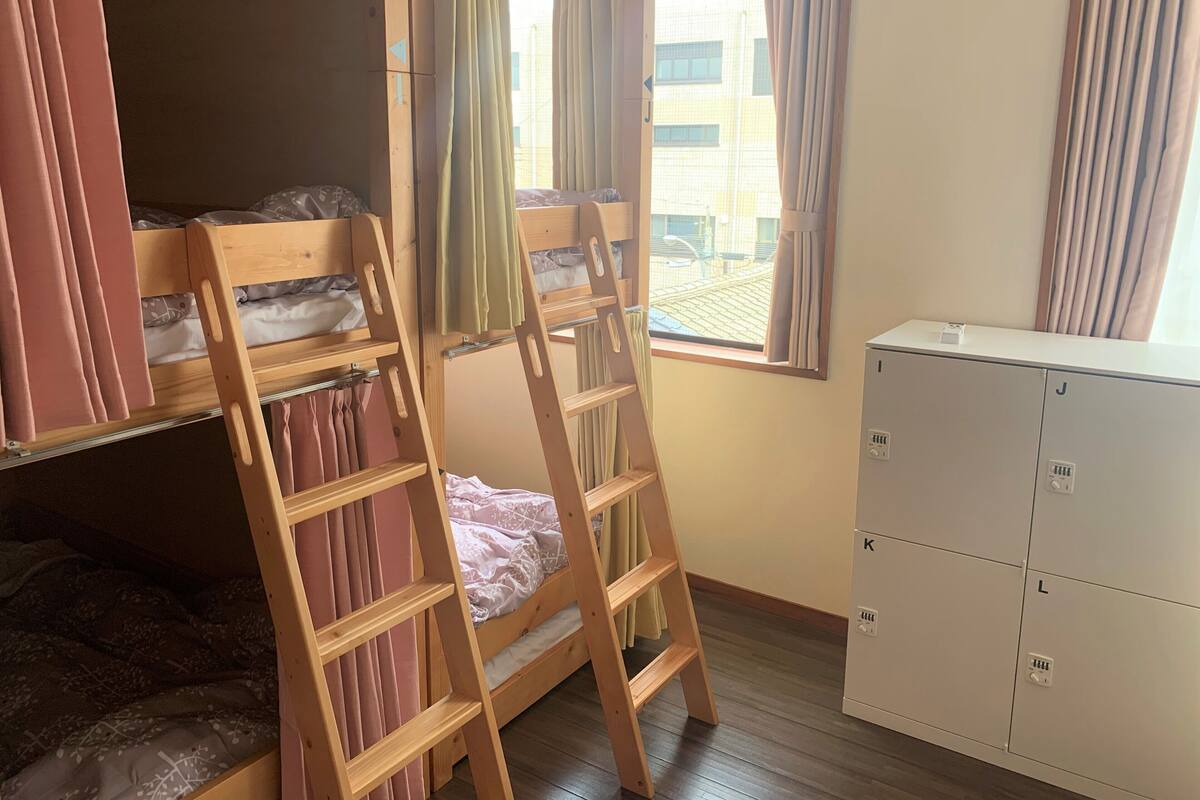Quarto com beliches, escada, janela com cortinas e um armário branco.